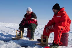 two guys trying their luck at ice fishing on a frozen lake